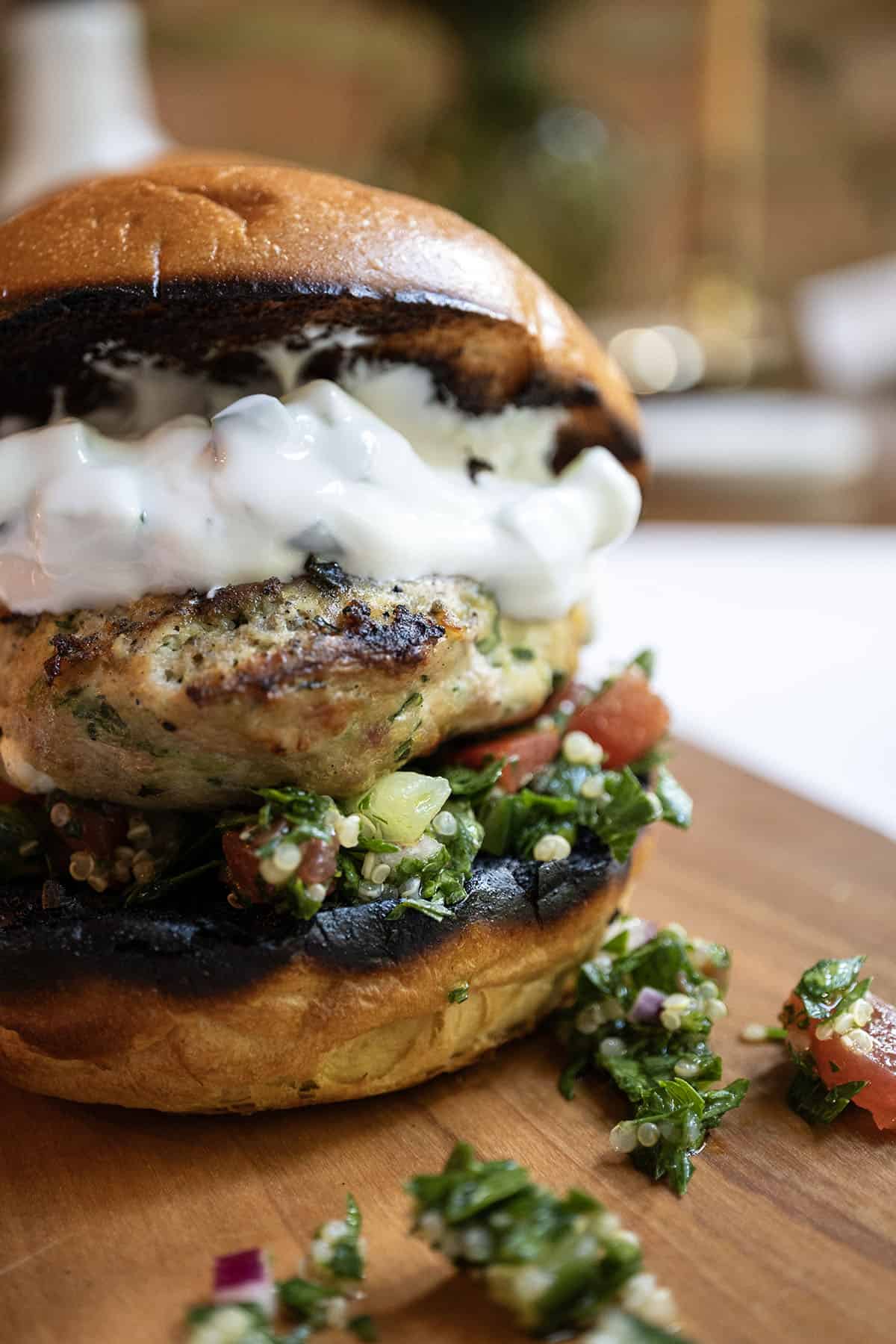 Greek chicken burger on a toasted bun with tabbouleh and topped with tzatziki.