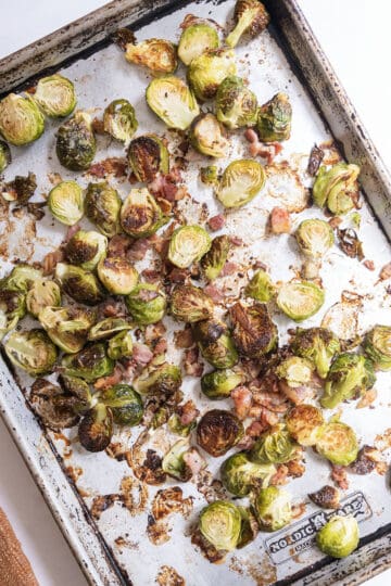 Roasted brussels sprouts and bacon on a baking tray.