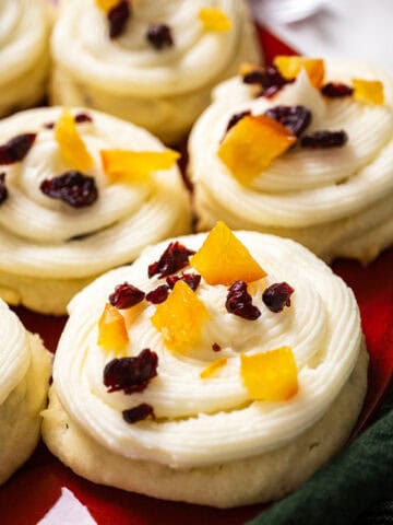 Cranberry and orange shortbread cookies topped with frosting and garnished with dried cranberries and candied oranges.