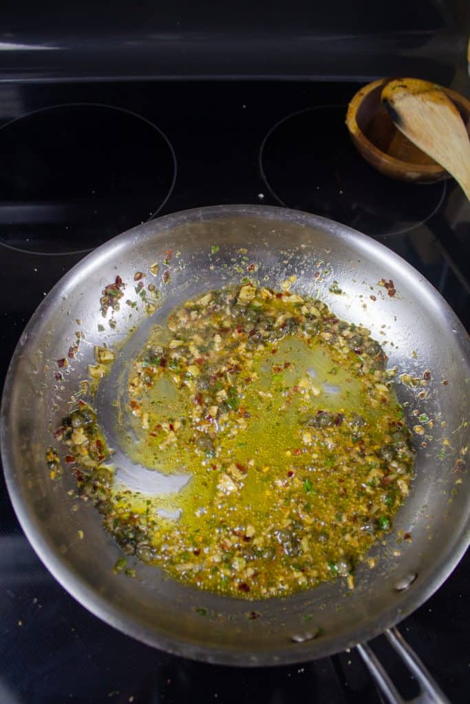 Garlic, Anchovy, capers, and parsley in olive oil in a pan on the stove