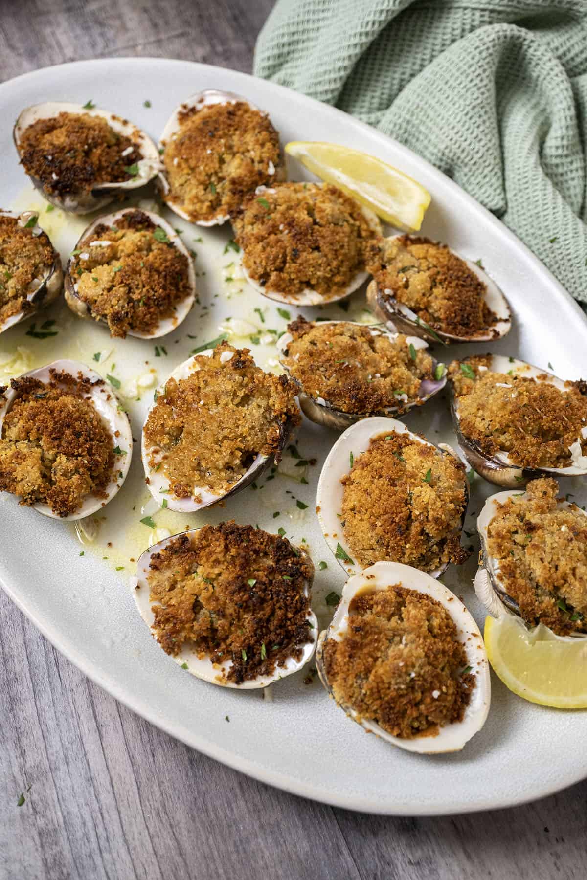 Baked clams on a plate with lemon garlic sauce underneath. 