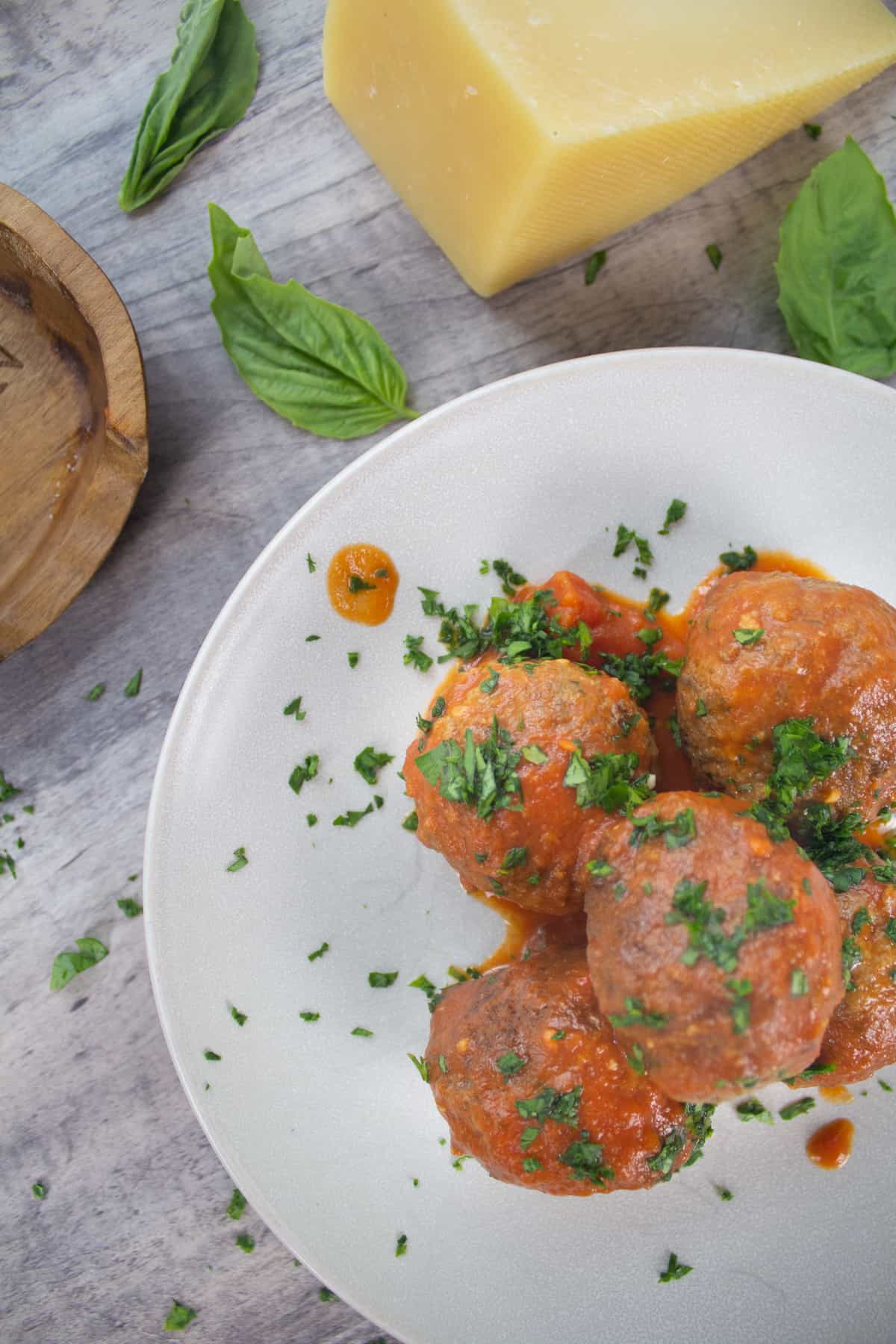 Meatballs served on a plate with fresh chopped parsley and garnished with basil and a block of parmesan cheese