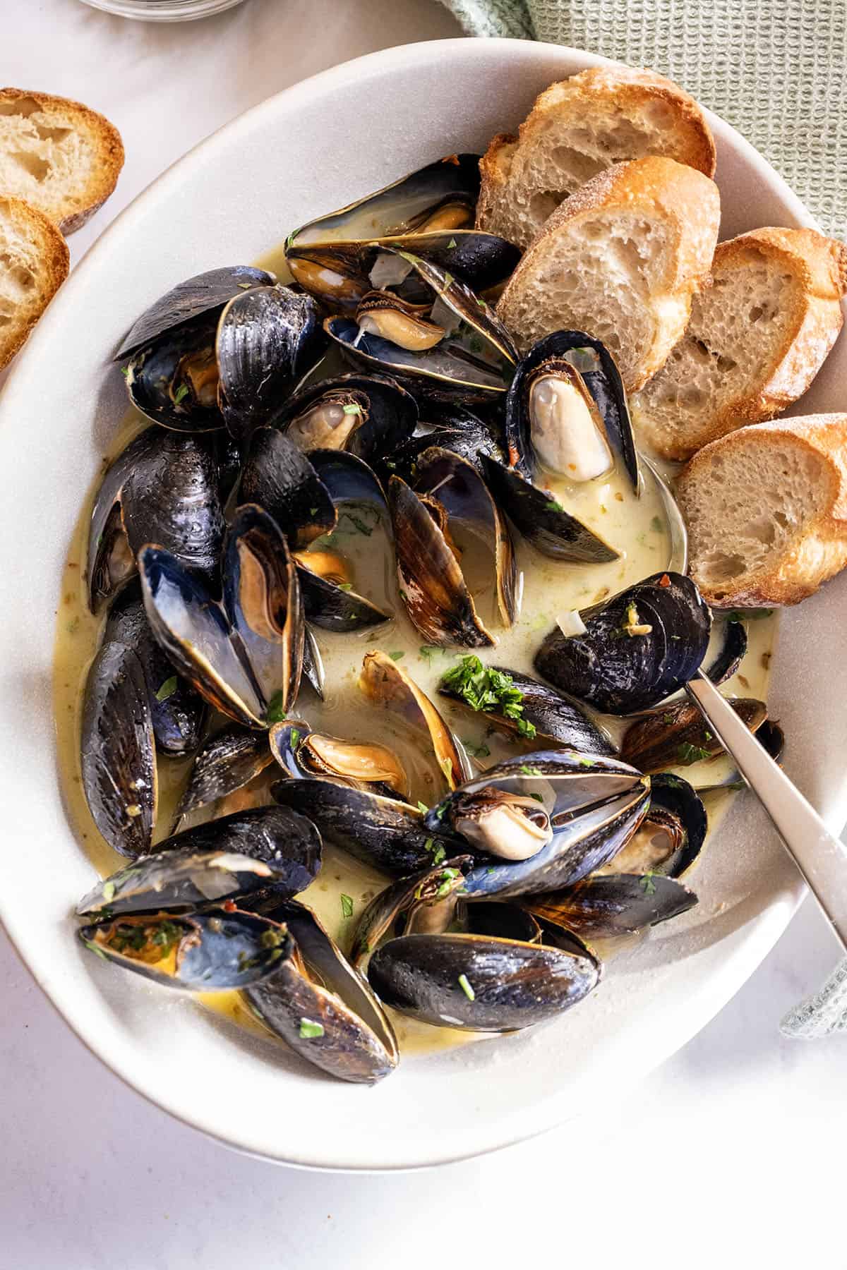 Steamed mussels in a serving bowl filled with white wine sauce and crostini on the side.