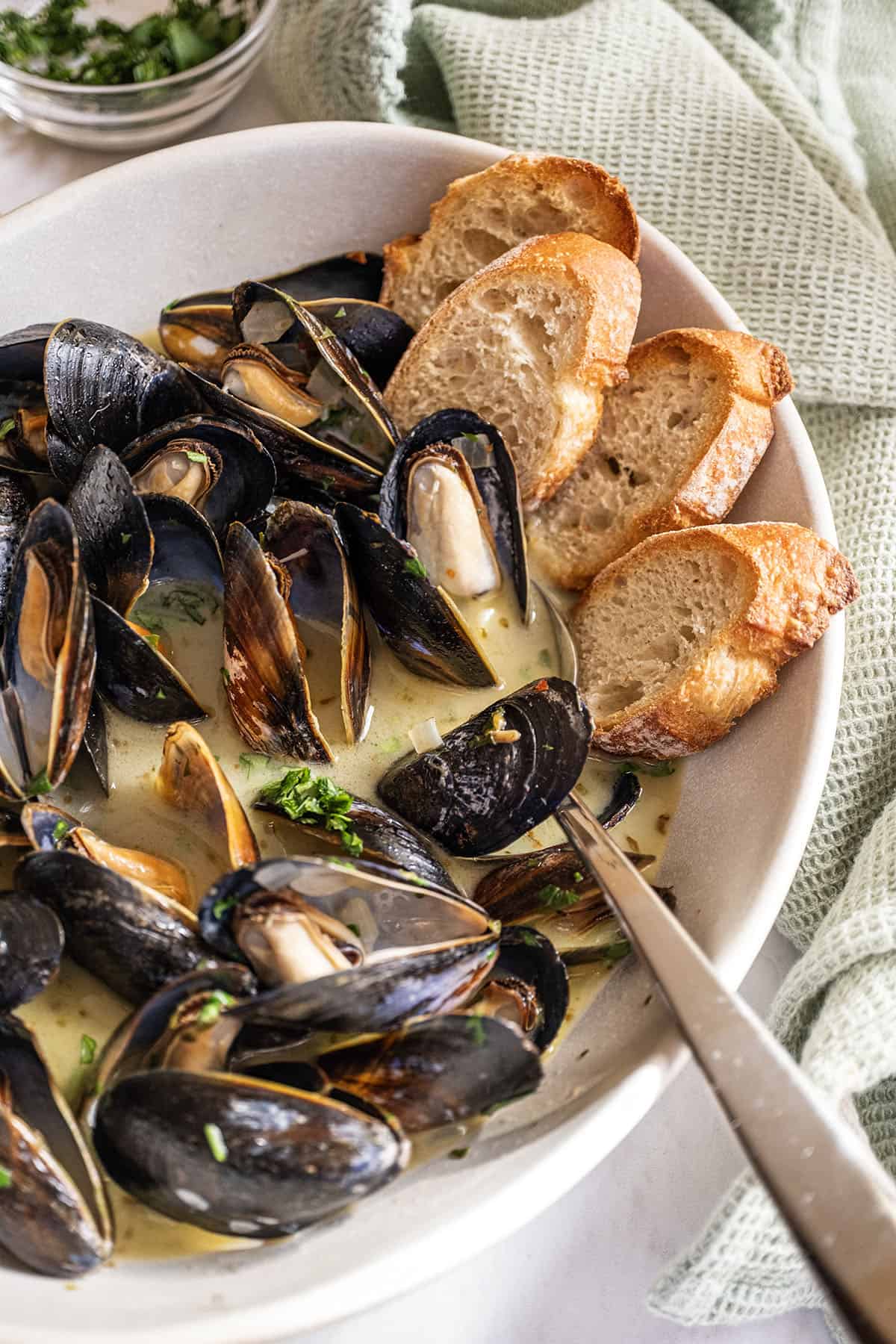 Steamed mussels in a serving bowl filled with white wine sauce and crostini on the side.