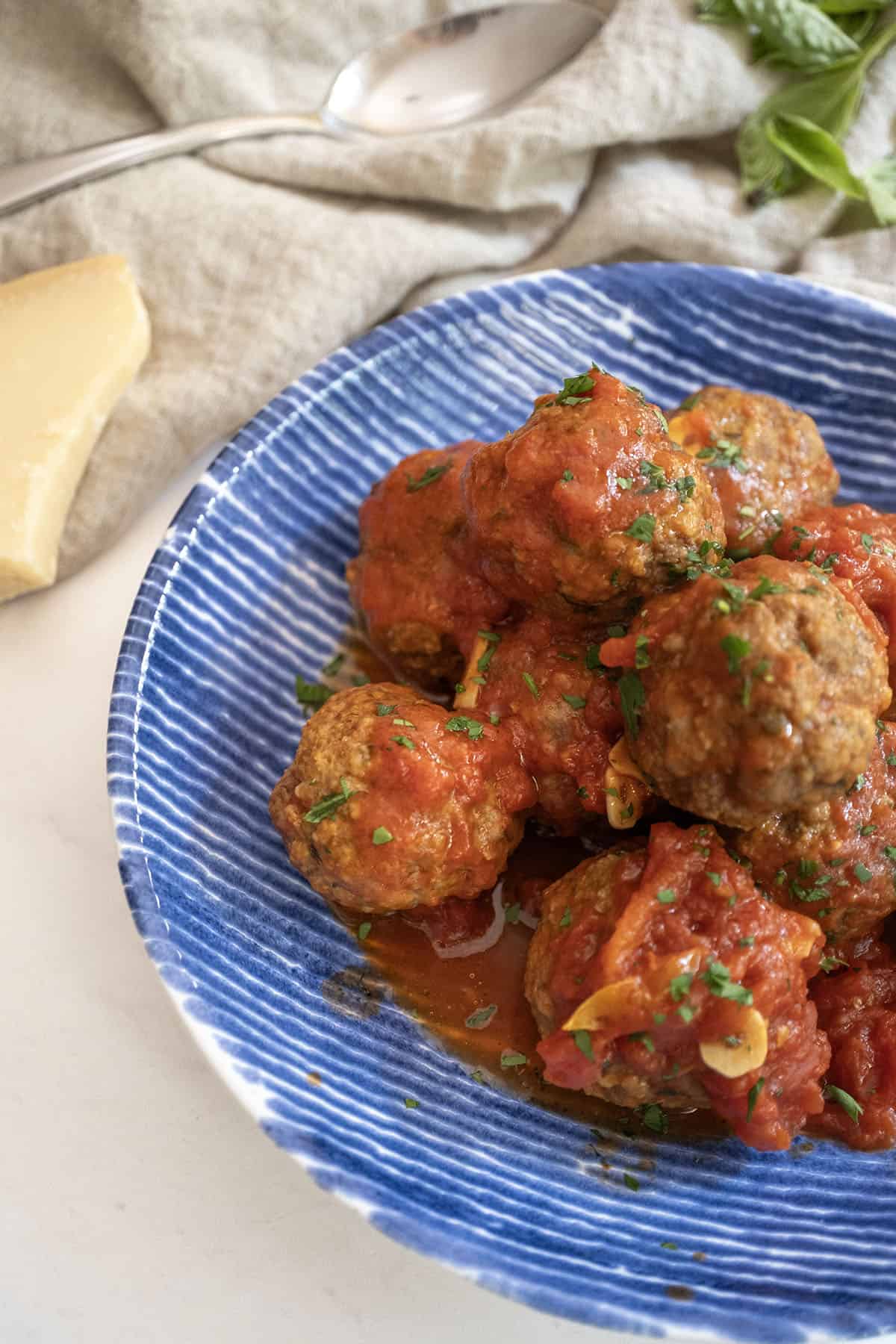 Meatballs covered in tomato sauce in a bowl with a block of parmesan cheese on the side.