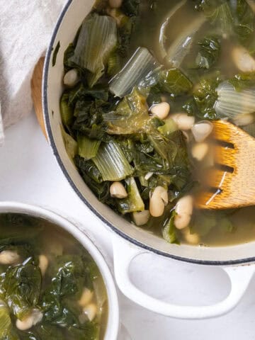 A dutch oven filled with escarole and beans along with a bowl of the same.