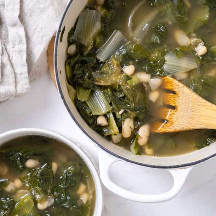 A dutch oven filled with escarole and beans along with a bowl of the same.