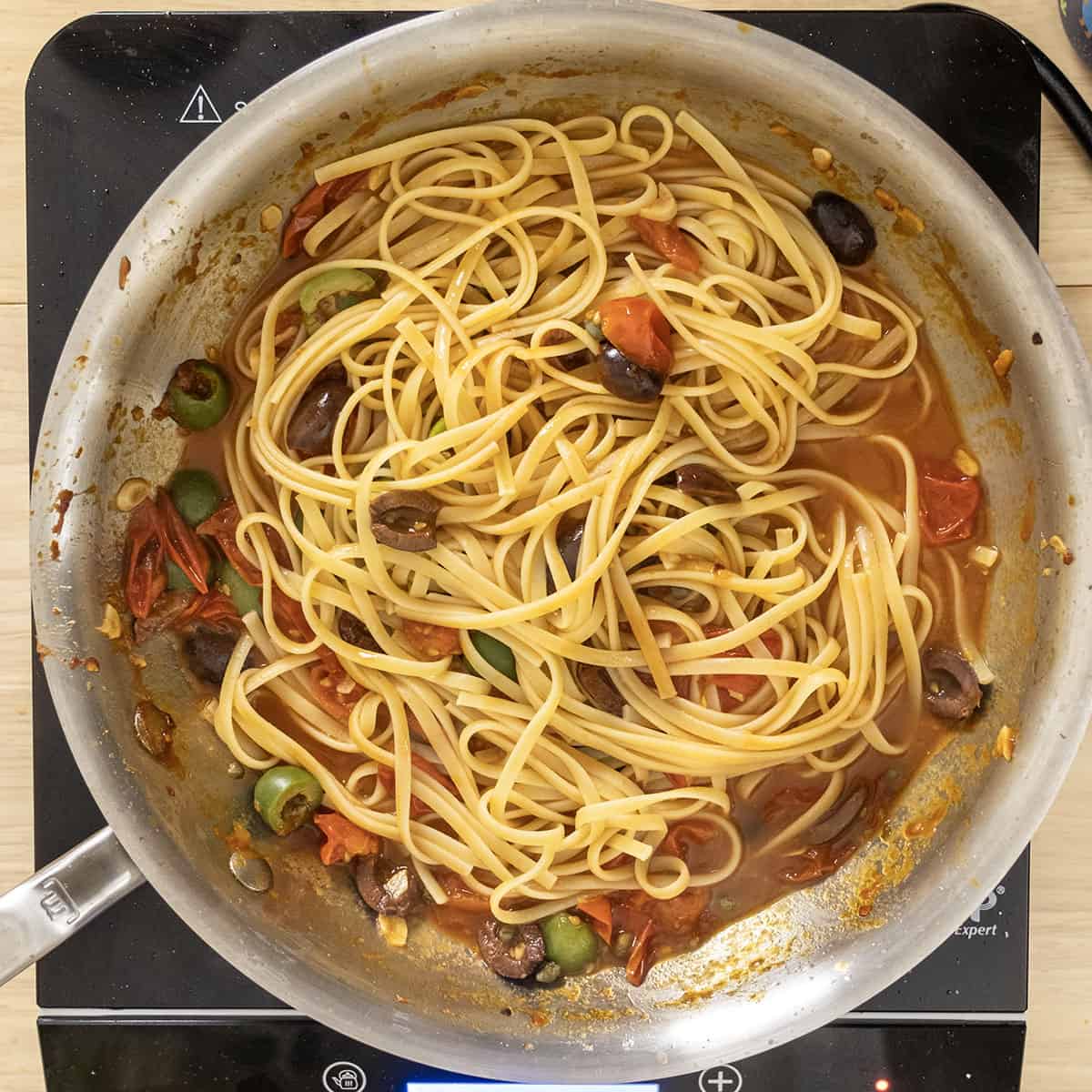 Pasta combined with puttanesca sauce in pan.