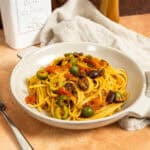 Linguine puttanesca topped with olives and capers in a bowl.