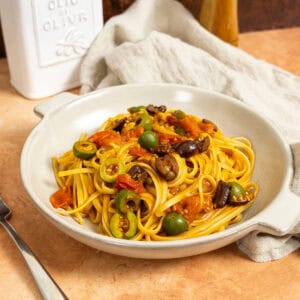 Linguine puttanesca topped with olives and capers in a bowl.