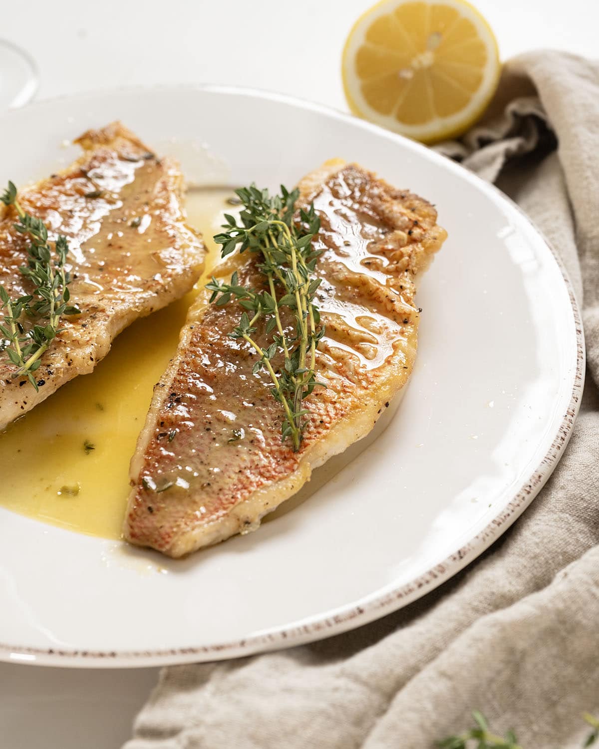 2 filets of pan seared vermillion snapper on a plate garnished with thyme sprigs.