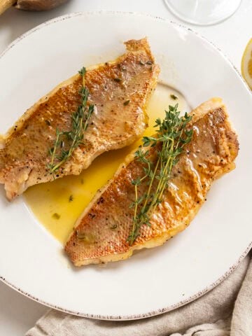 2 filets of pan seared vermillion snapper on a plate garnished with thyme sprigs.