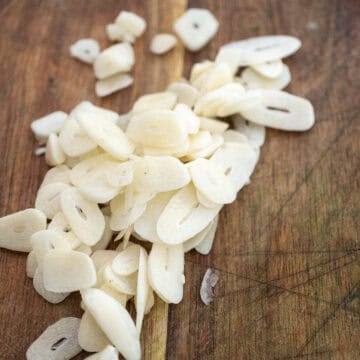 Garlic sliced thin on a cutting board.