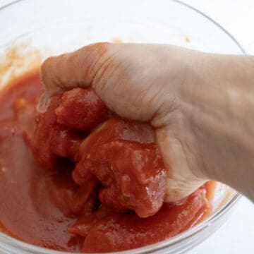 Hand crushing tomatoes in a bowl.