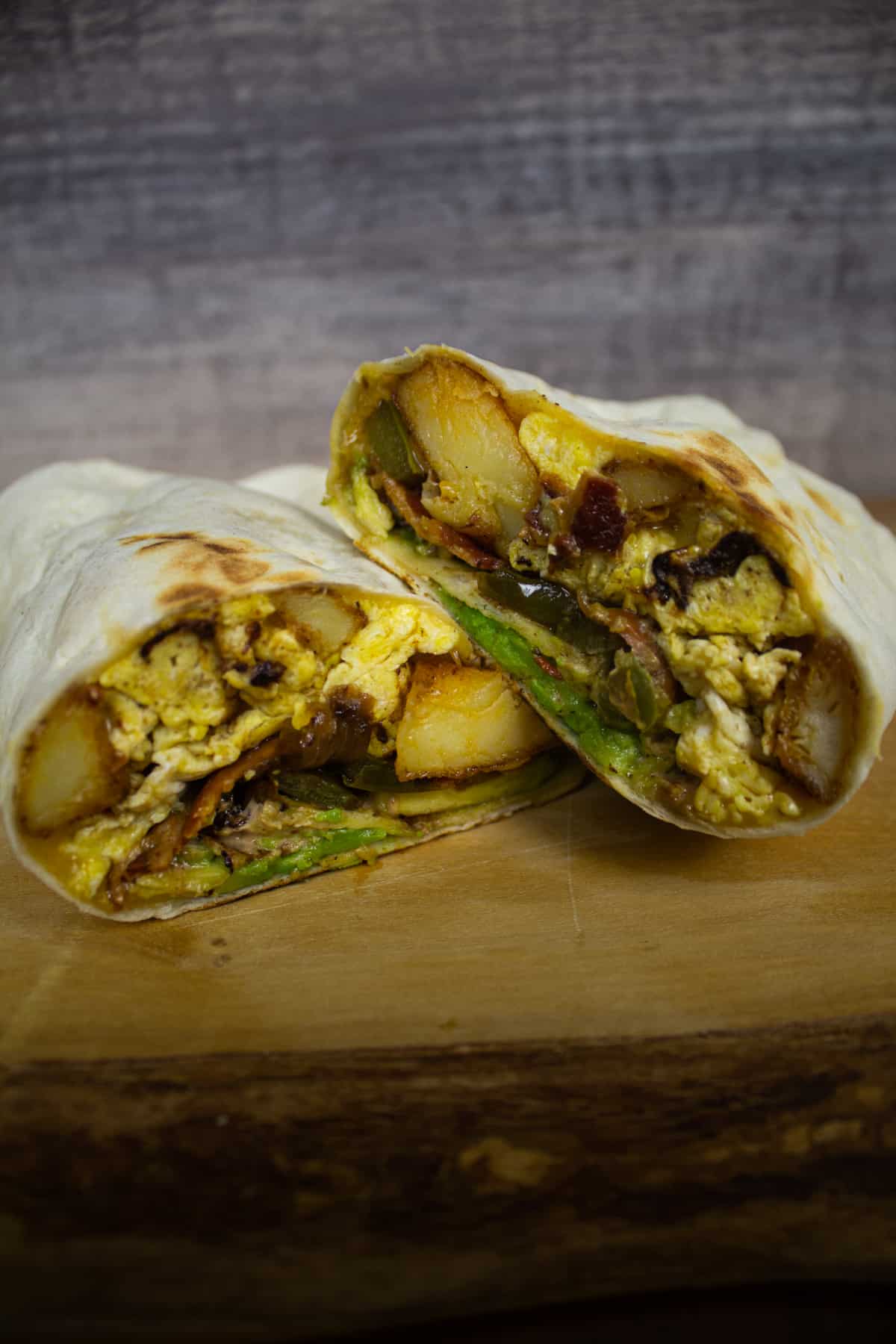 Southwest potato breakfast burrito cut in half showing potatoes, eggs, peppers and onions, bacon and cheese.