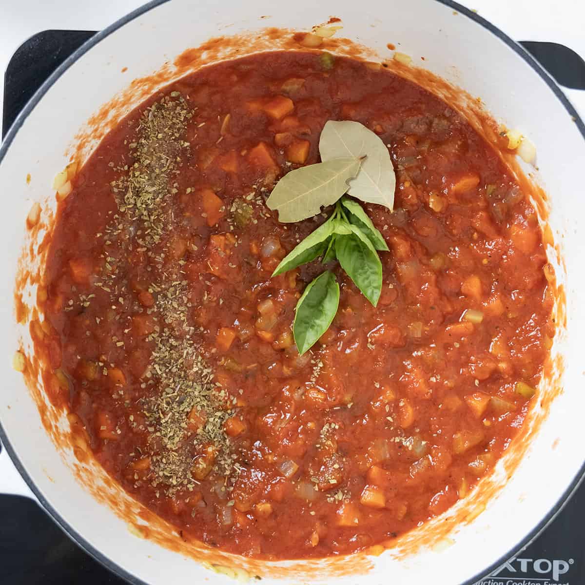 Crushed tomatoes, seasoning, basil, and bay leaves added to the vegetables.