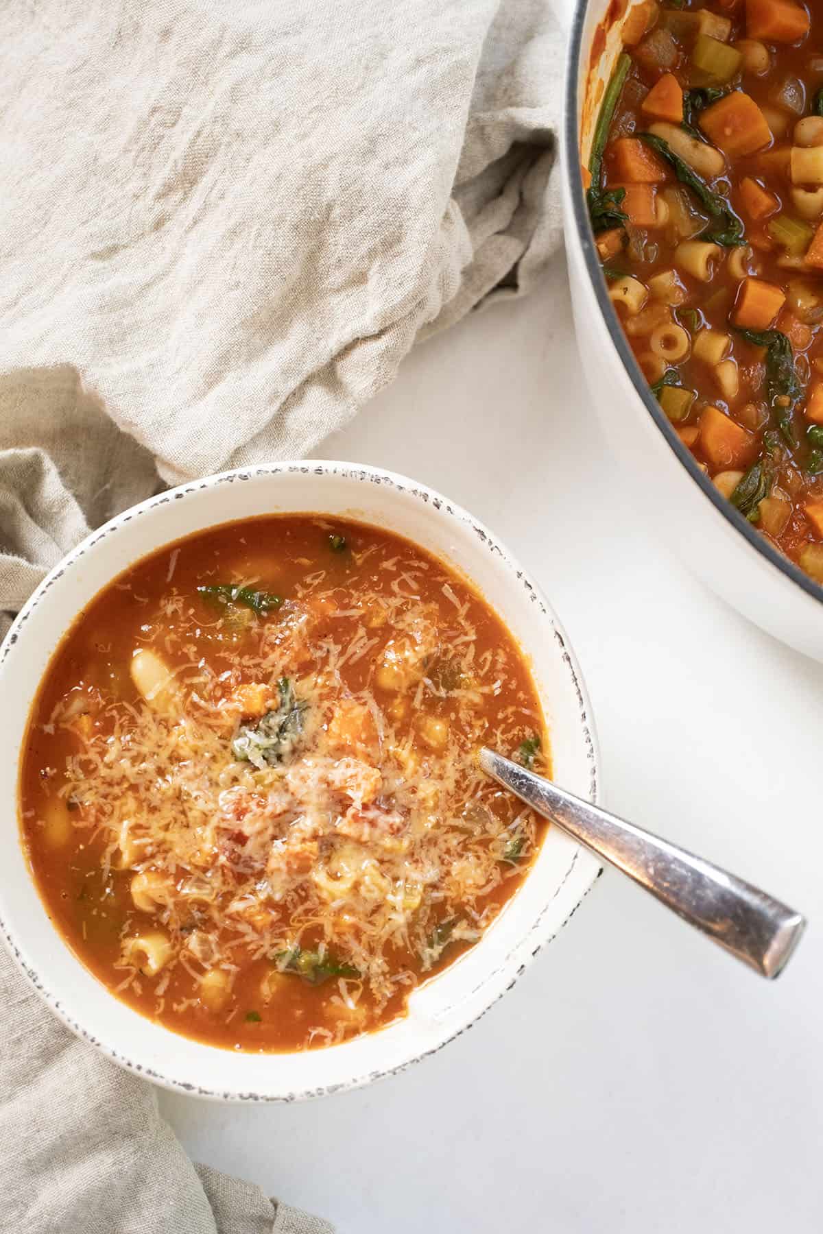 Pasta fagiolo topped with parmesan in a bowl next to the full pot of soup.