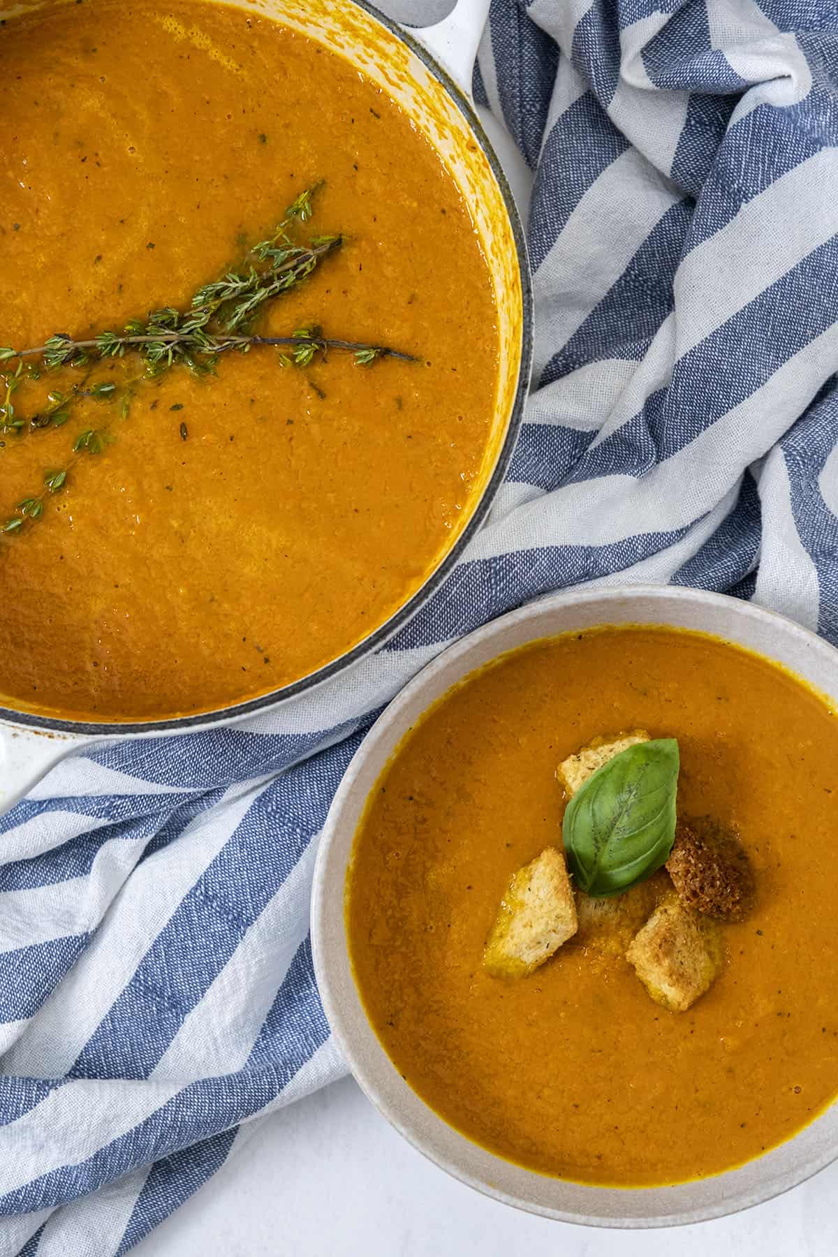 Roasted Carrot ginger soup in dutch oven and bowl, topped with crutons, thyme, and basil