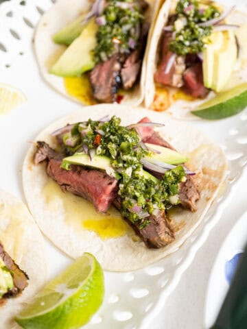 Chimichurri steak tacos on a plate with limes.