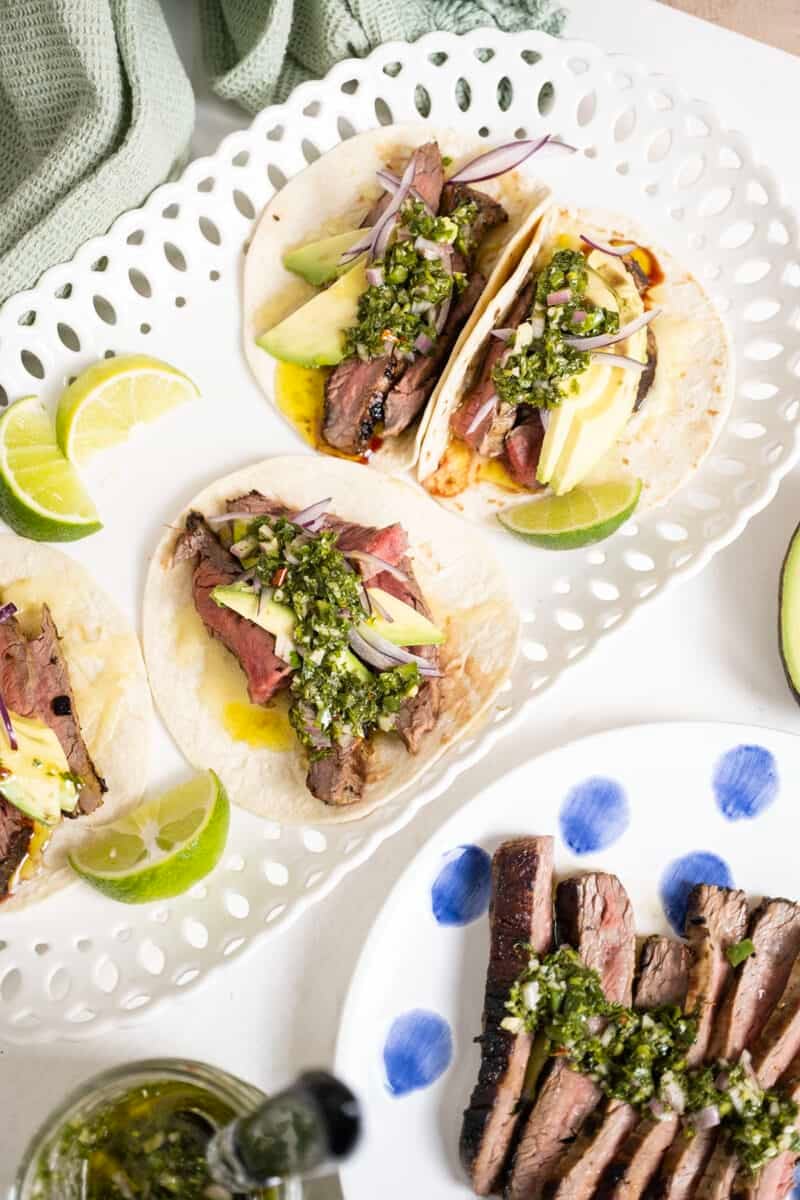 Chimichurri steak tacos on a plate with limes.