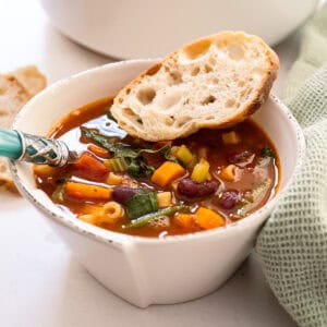 A bowl of minestrone with a piece of Italian bread.