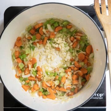 Carrots, celery, and onion sauteing in a pot with garlic.