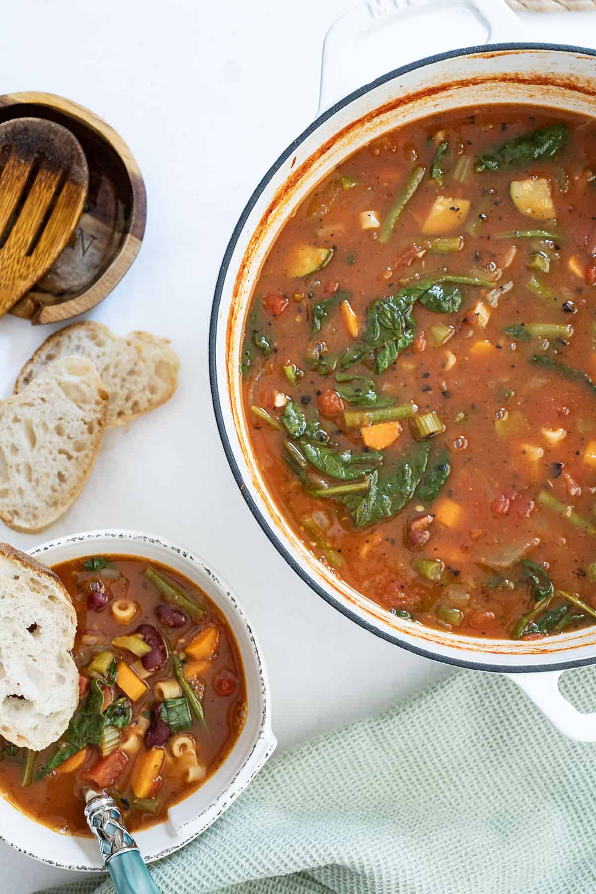 A bowl of minestrone with a piece of Italian bread next to the dutch oven filled with soup.