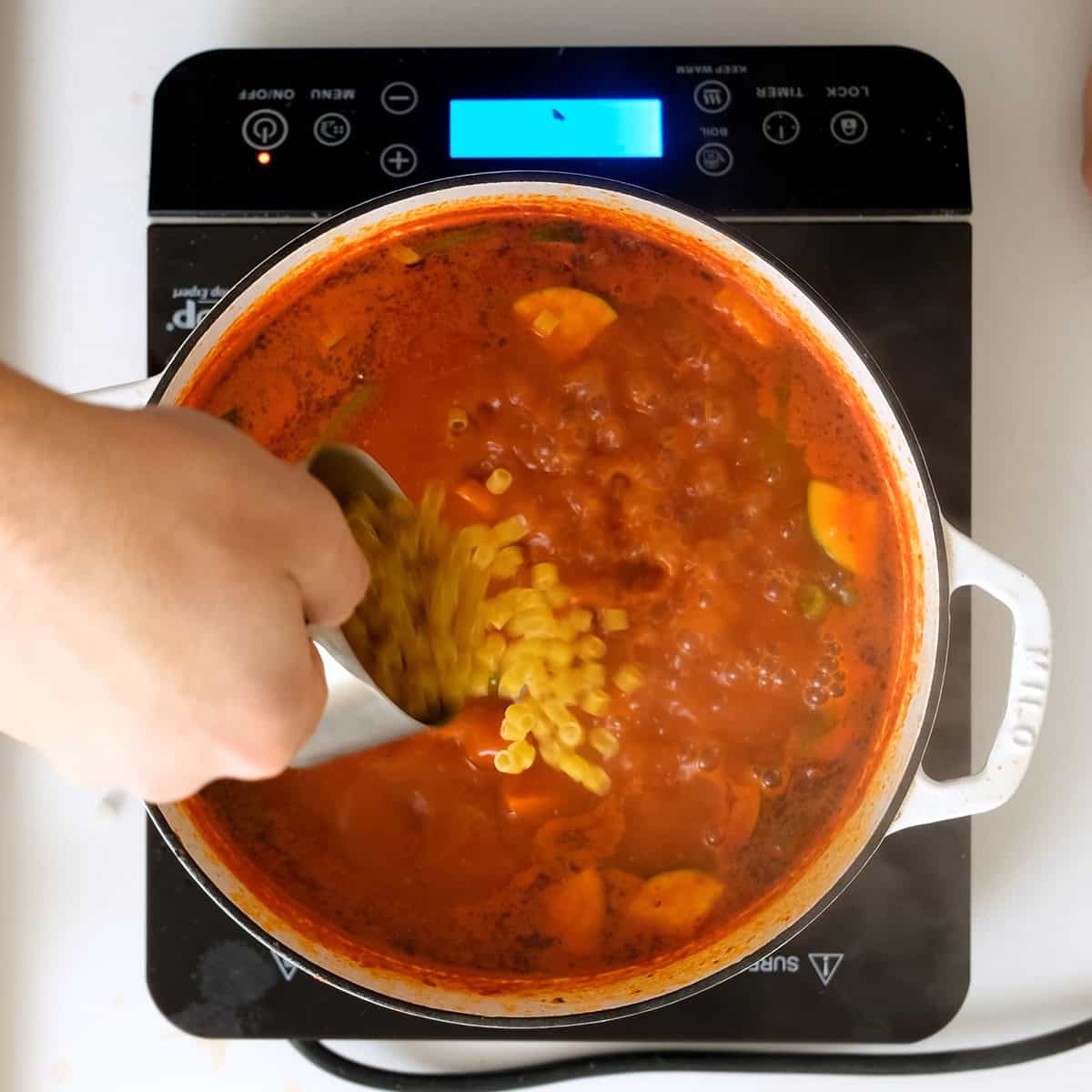 Pouring ditalini into the minestrone.