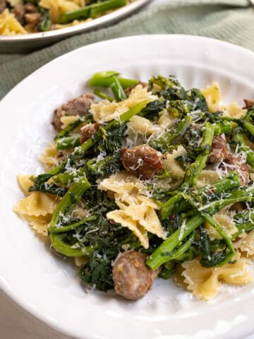 Farfalle with sausage and broccoli rabe, topped with parmesan on a plate.