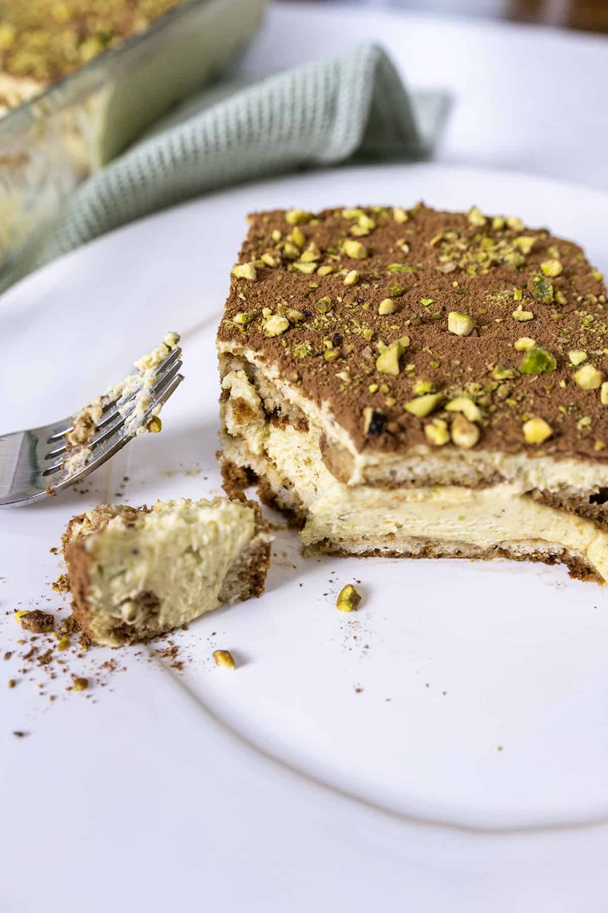 Pistachio Cream tiramisu on a plate with a forkful scooped out. 