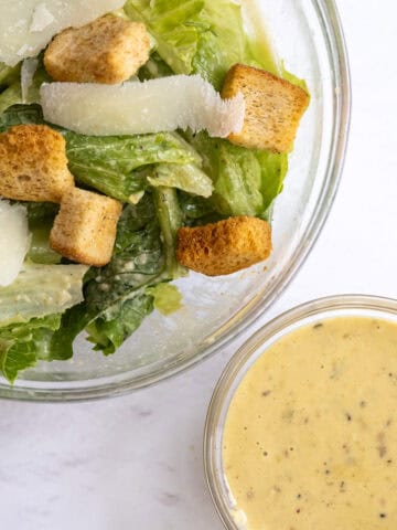 bowl of salad next to a small bowl of caesar dressing.