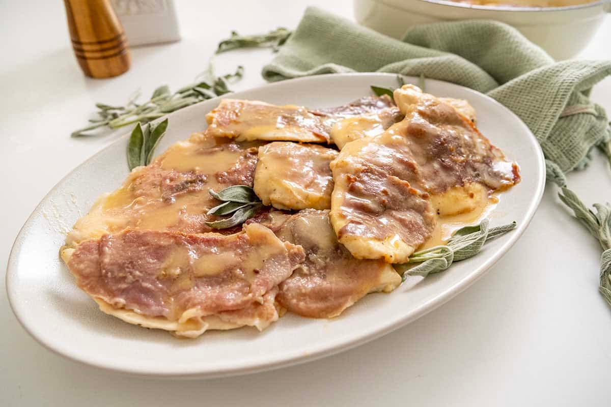 Chicken saltimbocca on a serving plate topped with fresh sage leaves. 