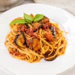 Pasta alla norma plated on a dish and garnished with basil.