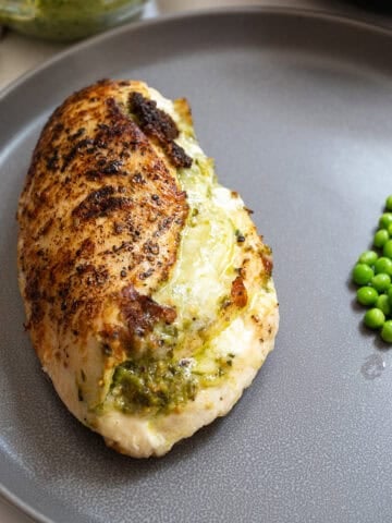 Pesto stuffed chicken on a plate with peas.