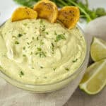 avocado lime crema in a glass bowl with limes and cilantro on side and chips in the crema.