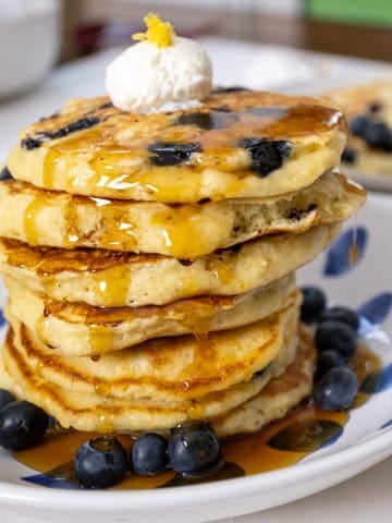 Lemon ricotta blueberry pancakes covered with syrup with a dollop of ricotta on top.