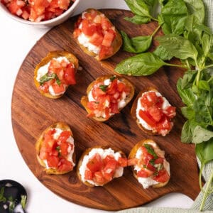 Toast topped with ricotta and bruschetta on a cutting board.