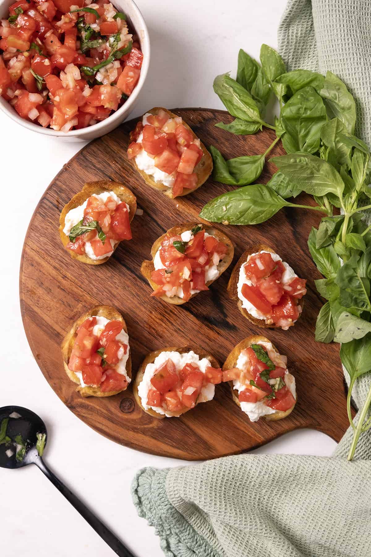 Toast topped with ricotta and bruschetta on a cutting board.