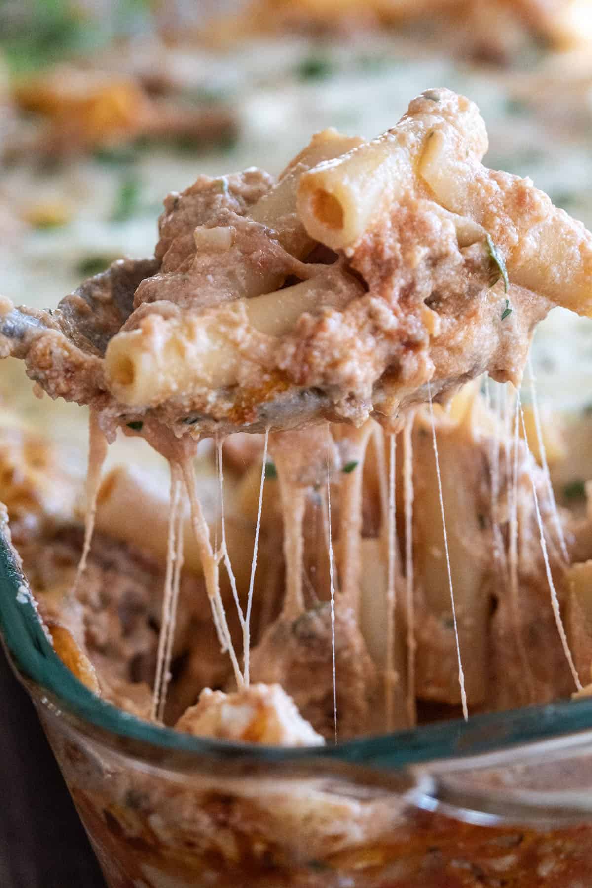 Cheesy pull of baked ziti on a spoon being scooped from the baking dish