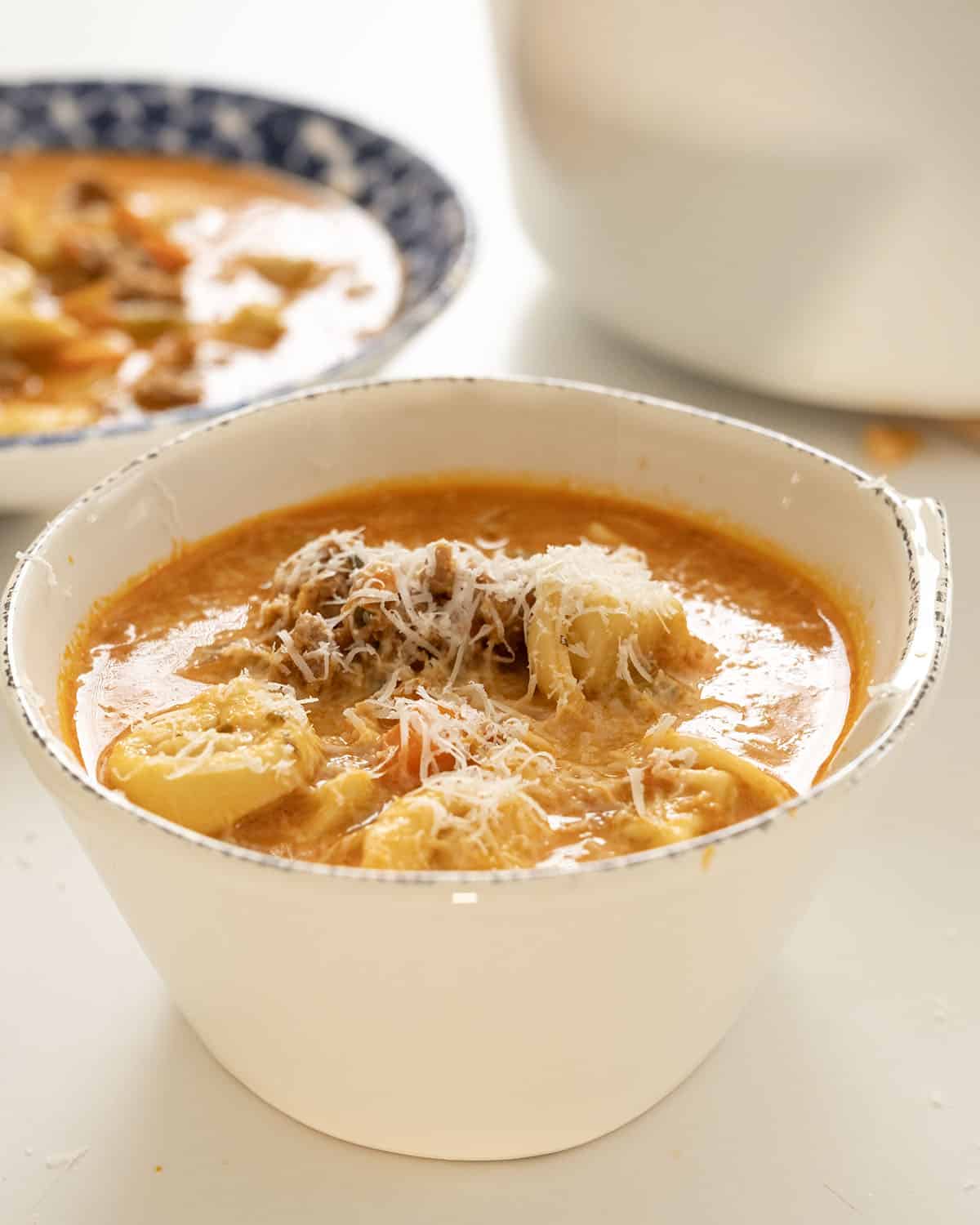 Rustic Italian tortellini soup with sausage in a bowl topped with parmesan cheese.
