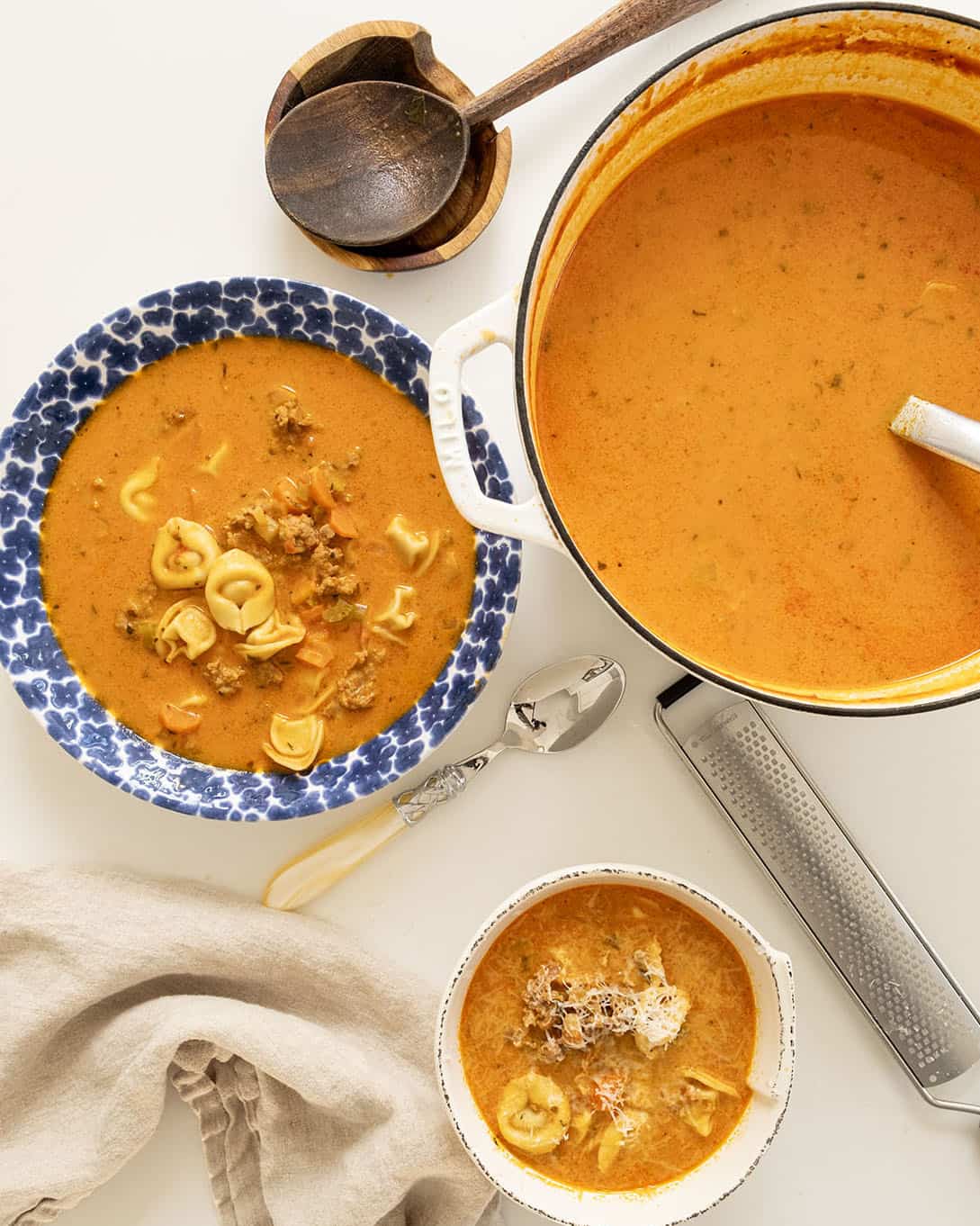 Rustic Italian tortellini soup with sausage in a bowl topped with parmesan cheese next to a pot of the soup.