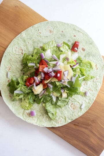 lettuce in wrap topped with red onion, roasted red pepper, and artichoke hearts