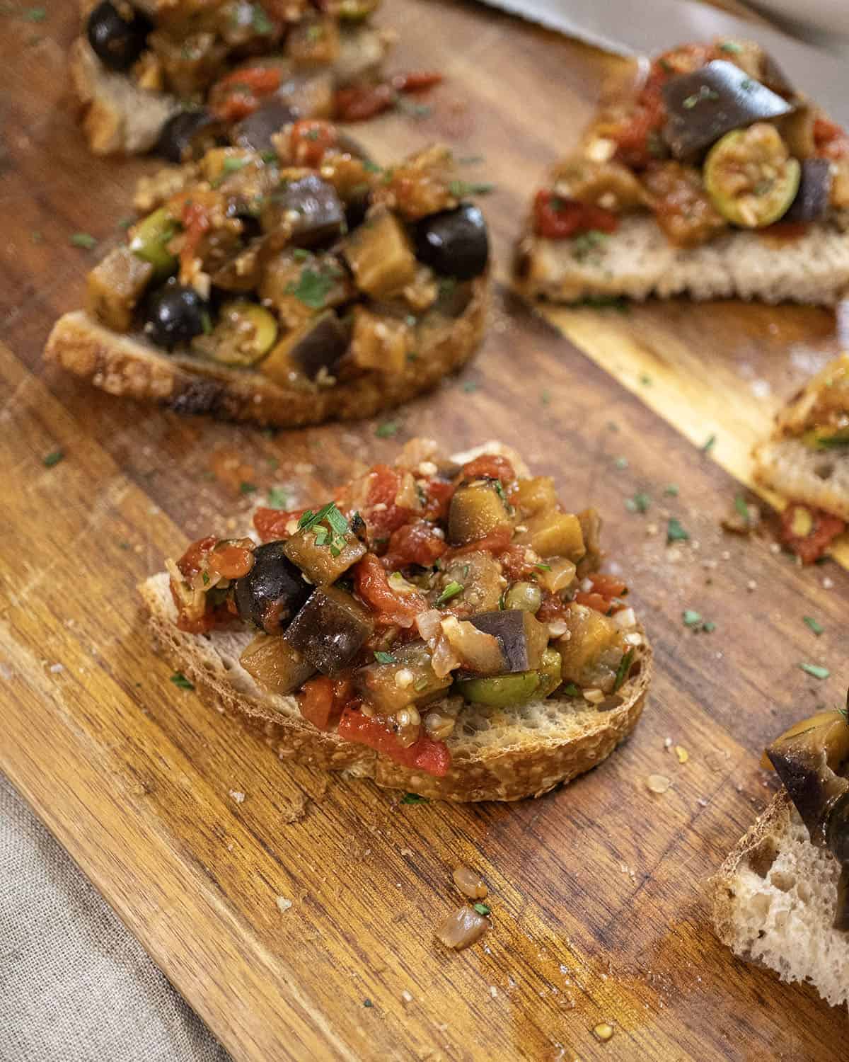 Eggplant caponata on crostini on a cutting board.