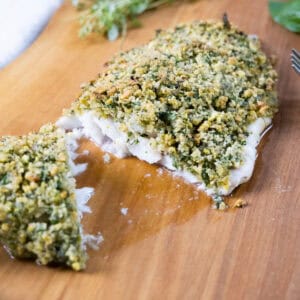 pistachio crusted sea bass cut in half on a cutting board.