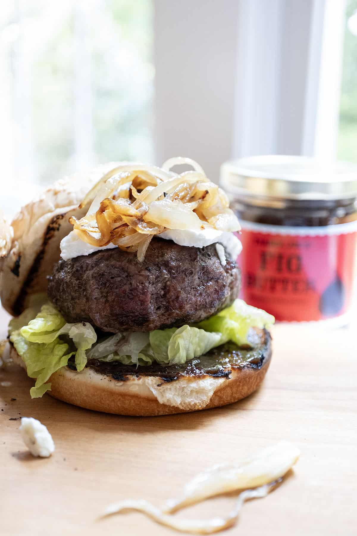 burger on a bed of lettuce with fig jam underneath, topped with goat cheese and caramelized onions.