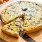 sausage and cheese quiche on a cutting board with one slice cut out.