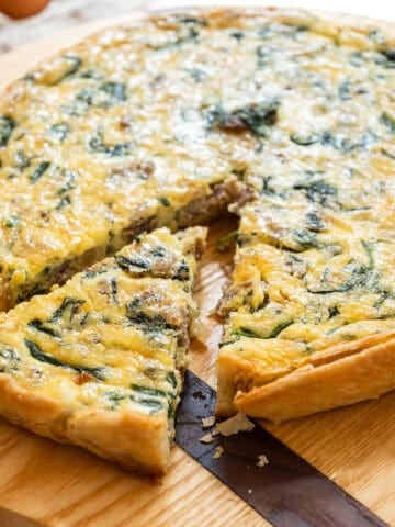 sausage and cheese quiche on a cutting board with one slice cut out.