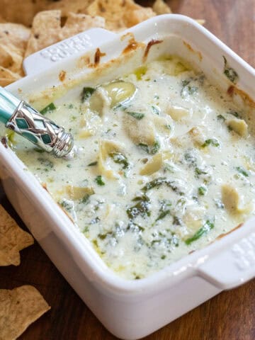 Spinach and artichoke dip in a dish with some tortilla chips next to it.