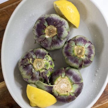 Artichokes soaking in lemon juice in a bowl.