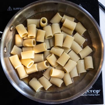 Adding halfway cooked pasta to the pan.